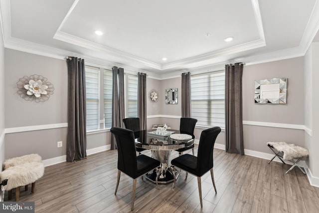 dining space with ornamental molding, light wood-style flooring, and a tray ceiling