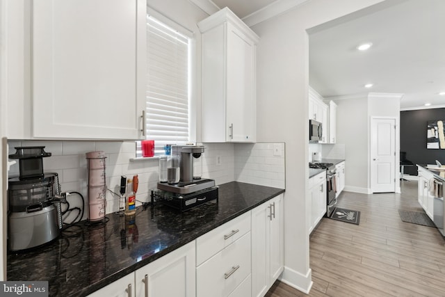 kitchen with white cabinets, appliances with stainless steel finishes, dark stone countertops, tasteful backsplash, and ornamental molding