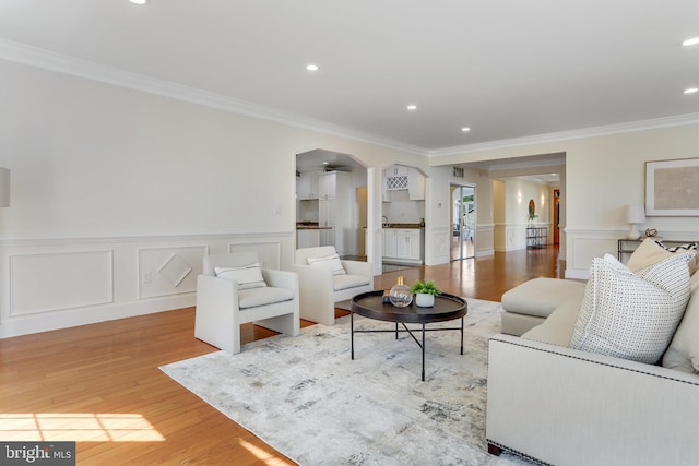 living room with crown molding, arched walkways, wainscoting, and wood finished floors
