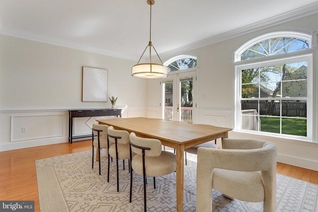 dining space with crown molding, light wood-type flooring, french doors, and a wainscoted wall