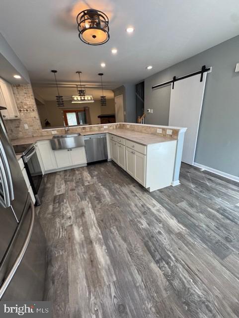 kitchen with white cabinets, dark wood-style flooring, appliances with stainless steel finishes, a barn door, and a sink