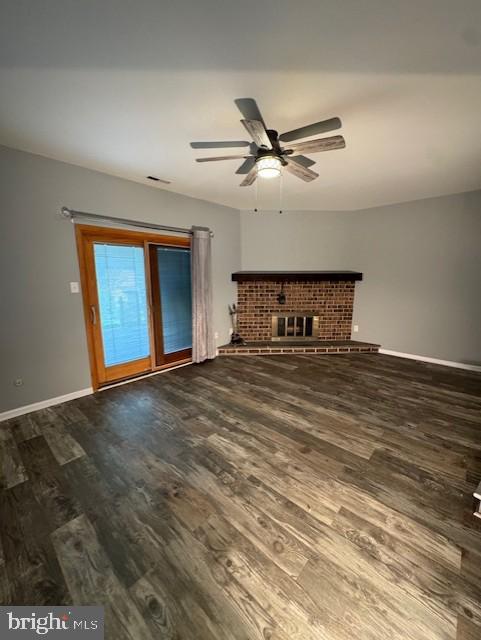 unfurnished living room with ceiling fan, visible vents, a brick fireplace, wood finished floors, and baseboards