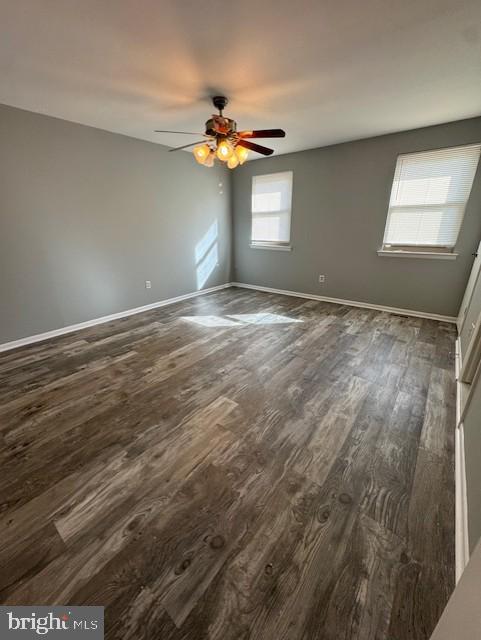 spare room featuring baseboards, ceiling fan, and dark wood-style flooring