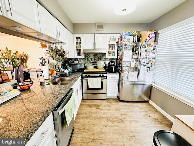 kitchen with appliances with stainless steel finishes, light wood finished floors, white cabinetry, under cabinet range hood, and glass insert cabinets