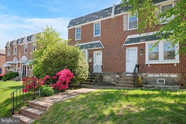 townhome / multi-family property featuring brick siding, a front yard, and entry steps