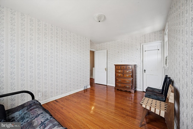 living area with wallpapered walls, wood finished floors, and visible vents