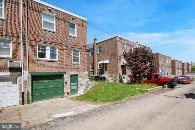 exterior space with driveway, a wall mounted air conditioner, a garage, brick siding, and stone siding