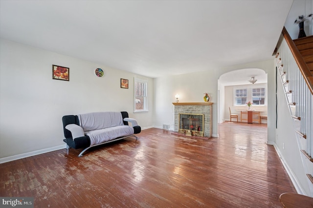 living room with arched walkways, baseboards, wood finished floors, and a fireplace