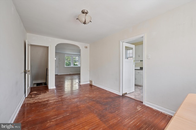 unfurnished dining area featuring arched walkways, baseboards, and hardwood / wood-style flooring