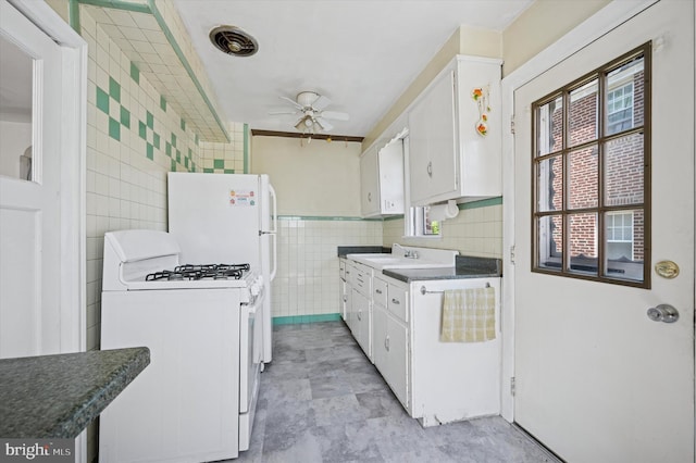 kitchen with a sink, gas range gas stove, white cabinetry, a ceiling fan, and tile walls