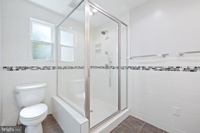 bathroom featuring tile walls, tile patterned flooring, a shower stall, a wainscoted wall, and toilet