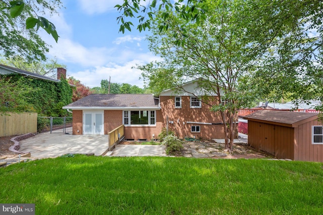 back of house with fence, brick siding, an outbuilding, a patio area, and a yard