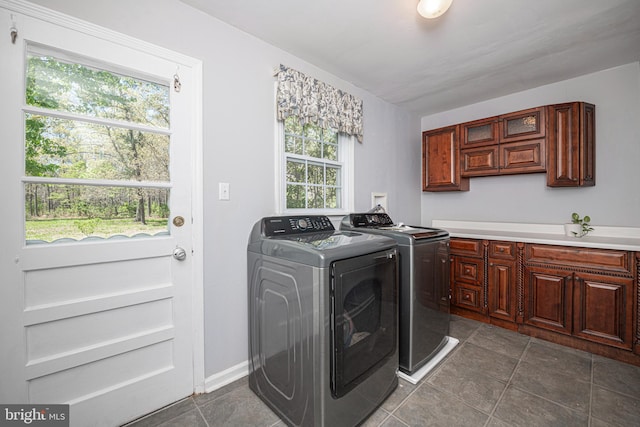 washroom with cabinet space, dark tile patterned flooring, a wealth of natural light, and washer and clothes dryer