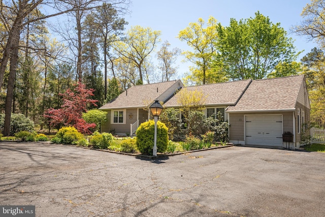 ranch-style home featuring a shingled roof, an attached garage, and aphalt driveway