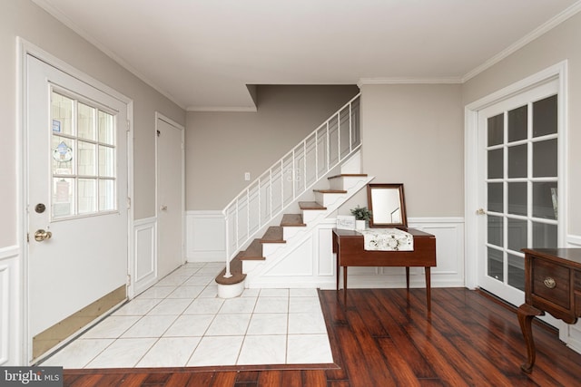 entrance foyer with stairway, a wainscoted wall, light wood finished floors, ornamental molding, and a decorative wall