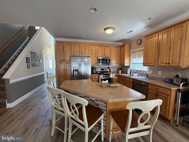 kitchen with visible vents, wood finished floors, a kitchen island, tasteful backsplash, and appliances with stainless steel finishes