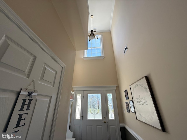 entryway featuring crown molding, a high ceiling, visible vents, and a notable chandelier