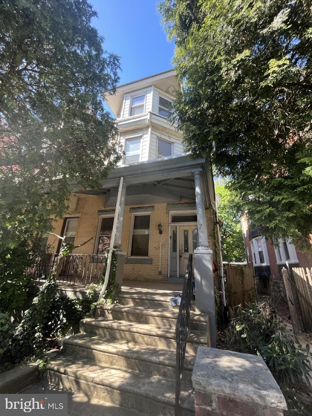 view of front facade featuring brick siding, covered porch, and stairway