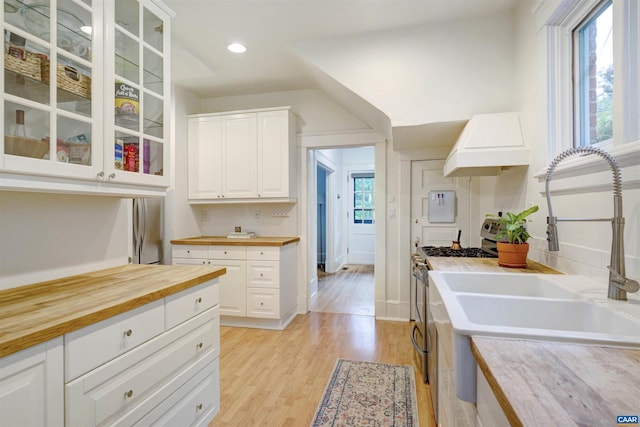 883 Locust Ave, Charlottesville, VA 22902 - kitchen featuring stainless steel range with gas stovetop, wood counters, custom range hood, light wood-type flooring, and glass insert cabinets