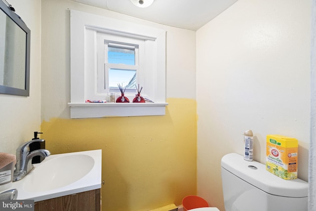 half bath with toilet, baseboards, and vanity