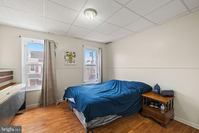 bedroom with a drop ceiling, multiple windows, and light wood-type flooring