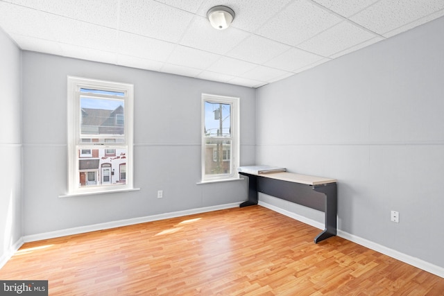 spare room featuring a paneled ceiling, baseboards, plenty of natural light, and light wood-style flooring