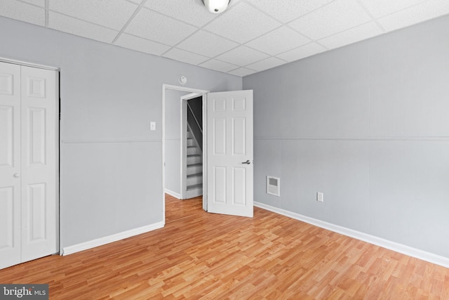 unfurnished bedroom featuring baseboards, visible vents, a paneled ceiling, and light wood finished floors