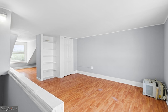 bonus room with baseboards, built in shelves, and light wood-style flooring