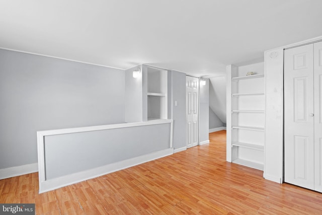below grade area with baseboards, built in features, and wood finished floors