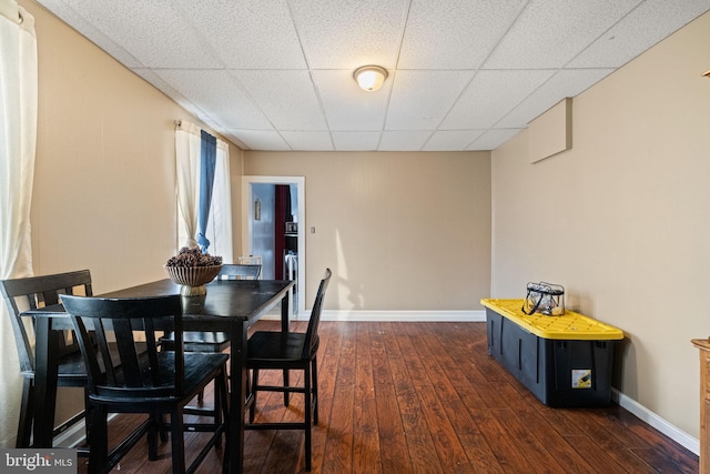 dining area featuring baseboards, dark wood-style floors, and a drop ceiling