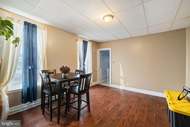 dining space featuring dark wood-style flooring, baseboards, and a paneled ceiling