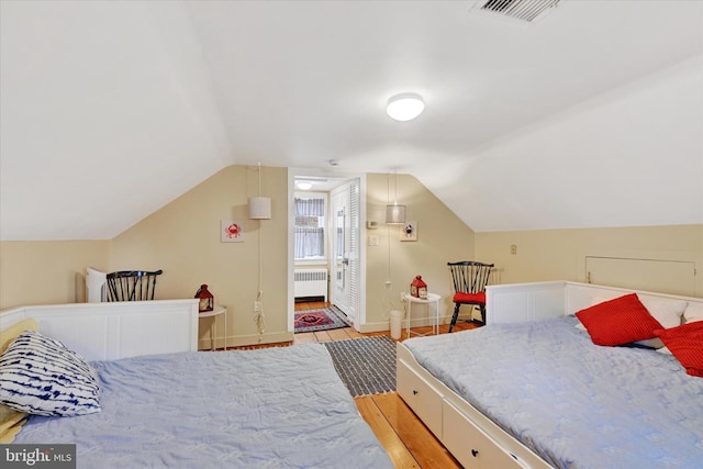 bedroom with radiator heating unit, visible vents, vaulted ceiling, light wood-style flooring, and baseboards