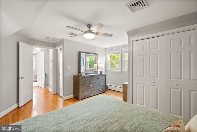 bedroom featuring a baseboard radiator, light wood finished floors, a closet, and baseboards