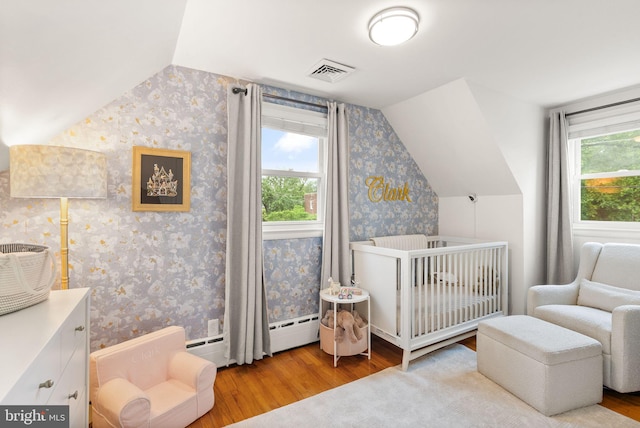 bedroom featuring wallpapered walls, wood finished floors, vaulted ceiling, multiple windows, and a crib