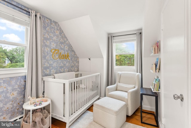 bedroom with wallpapered walls, a nursery area, wood finished floors, and vaulted ceiling