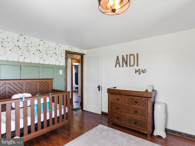 bedroom featuring baseboards, a decorative wall, wallpapered walls, and wood finished floors