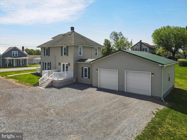 back of house with a garage, gravel driveway, a deck, a chimney, and a lawn