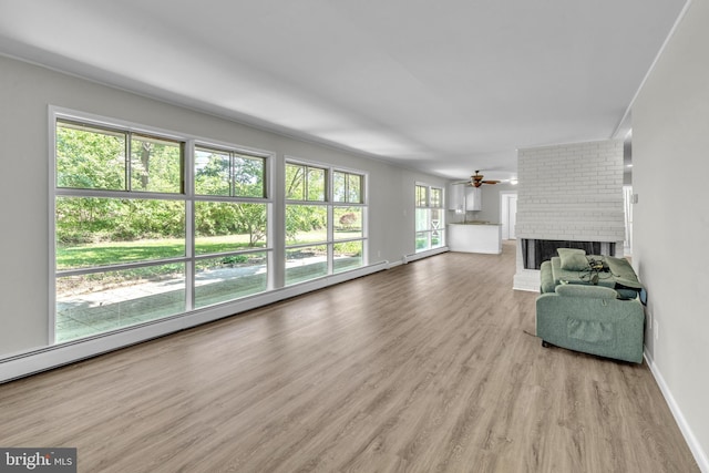 living room featuring wood finished floors, a fireplace, a ceiling fan, a baseboard heating unit, and baseboards