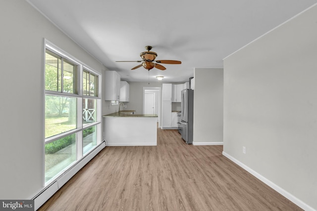 unfurnished living room featuring baseboard heating, light wood-type flooring, baseboards, ceiling fan, and a sink