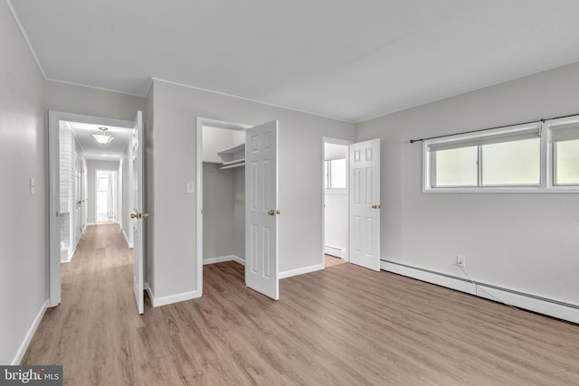 unfurnished bedroom with light wood-style floors, a baseboard heating unit, baseboards, a spacious closet, and a closet