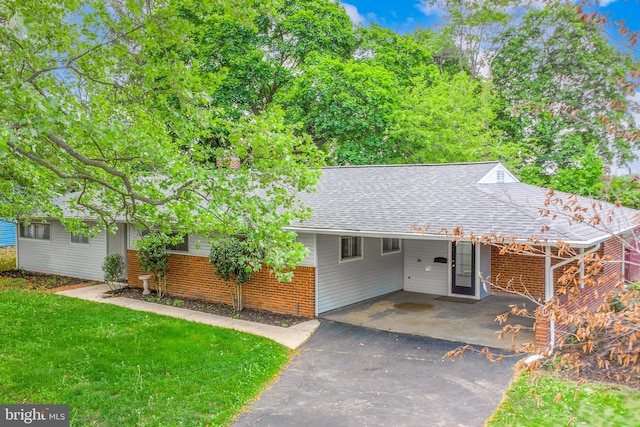 ranch-style home featuring asphalt driveway, a shingled roof, a carport, a front lawn, and brick siding