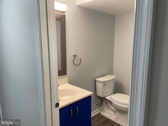 half bath with toilet, baseboards, wood finished floors, and vanity