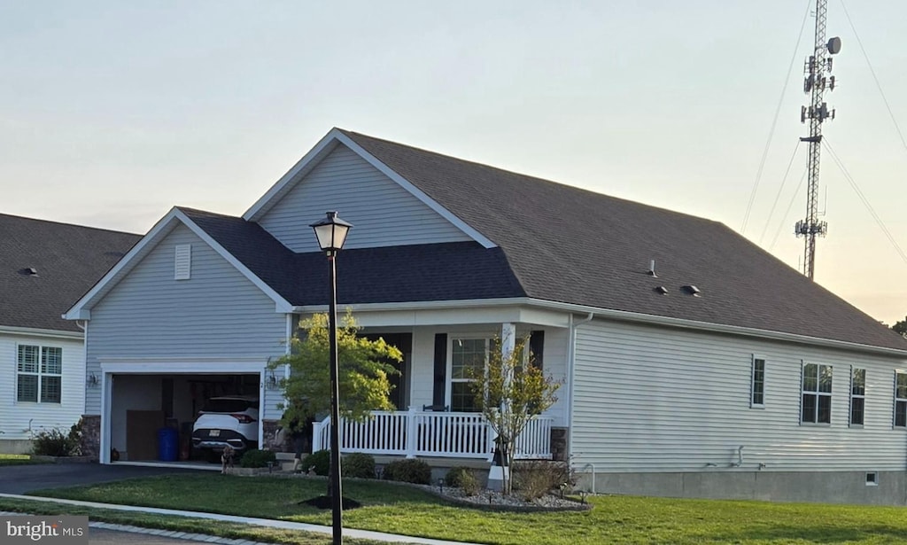 property exterior at dusk featuring a shingled roof, a garage, covered porch, a yard, and driveway