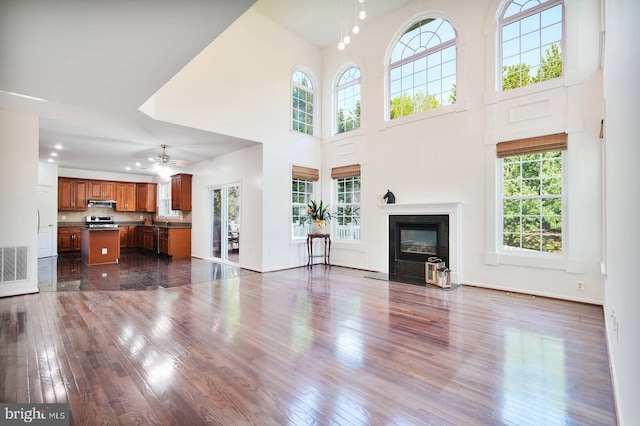 unfurnished living room featuring dark wood-type flooring, a high end fireplace, a towering ceiling, a ceiling fan, and a sink