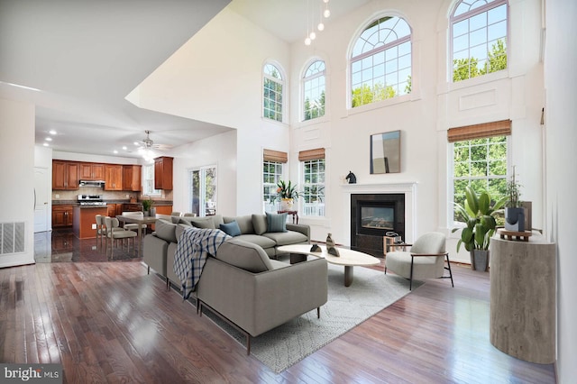 living room with dark wood finished floors, a high ceiling, a glass covered fireplace, and a ceiling fan