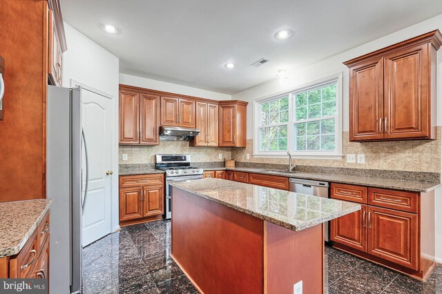 kitchen with stainless steel appliances, under cabinet range hood, granite floors, a center island, and recessed lighting