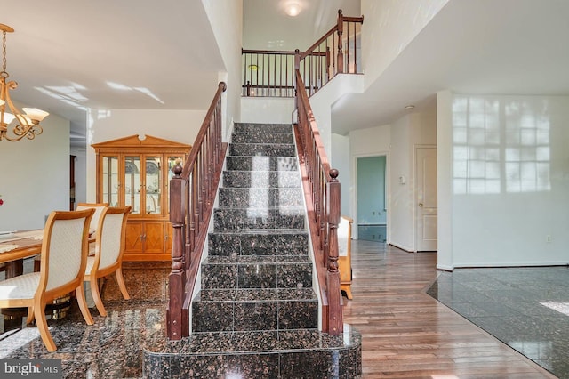 staircase with a chandelier, wood finished floors, and a towering ceiling