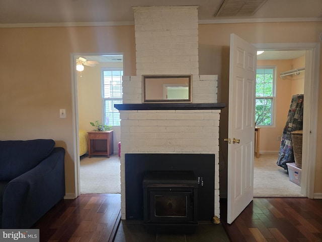 detailed view of wood finished floors, ornamental molding, baseboards, a wood stove, and ceiling fan