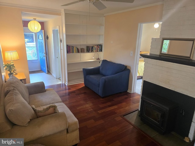 living room with ceiling fan, a wood stove, wood finished floors, ornamental molding, and baseboards