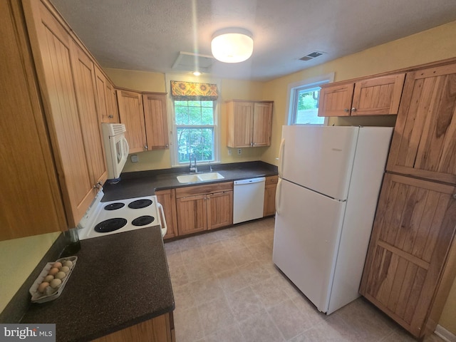 kitchen with white appliances, a sink, dark countertops, and brown cabinets